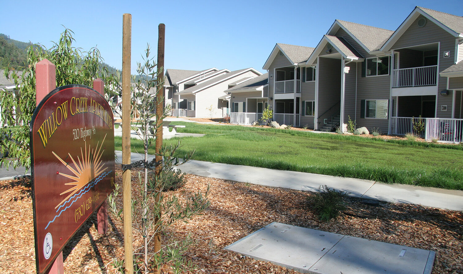 A well-maintained apartment complex with multiple two-story buildings on a sunny day. The complex features landscaped grounds and a sign in the foreground that reads Willow Creek Apartments.